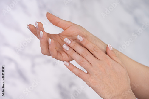 Beautiful female hands with french manicure on nails. Soft skin  skincare  beauty treatment concept. Young woman applying cream or lotion onto graceful hands with slender fingers on light background