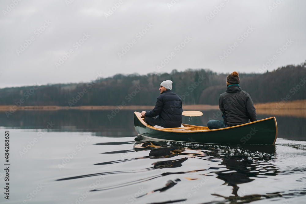 Two people in a green canoe along the calm lake in late autumn or early spring. Paddling lifestyle, enjoying tranquil and calm water and beautiful scenery