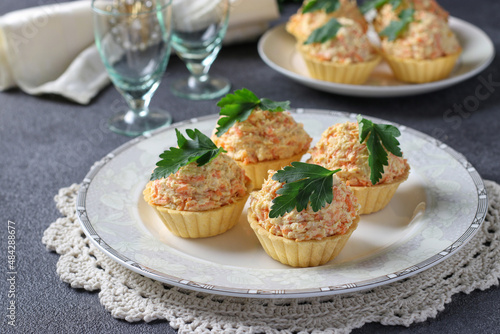 Tartlets with cheese, chicken and carrots garnished with parsley on a gray background