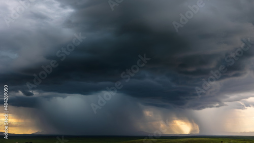 A dramatic monsoon storm with heavy rainfall over an open green field at sunset.