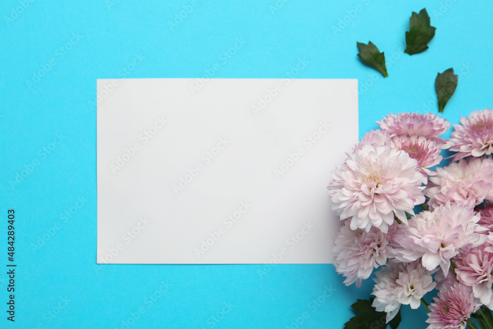 Beautiful chrysanthemum flowers and blank card on light blue background, flat lay. Space for text