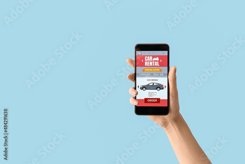 Female hand and mobile phone with open car rent app on blue background