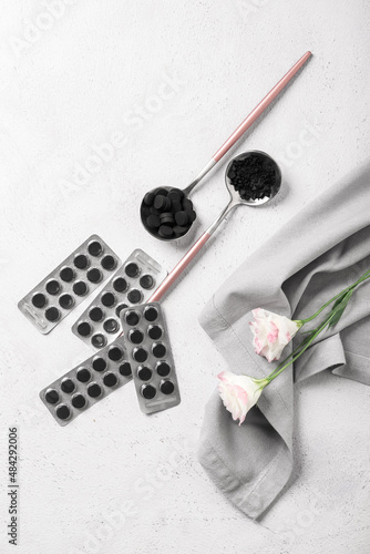 Activated carbon pills, napkin and flowers on light background