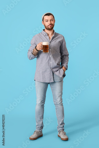 Young bearded man with glass of beer on blue background