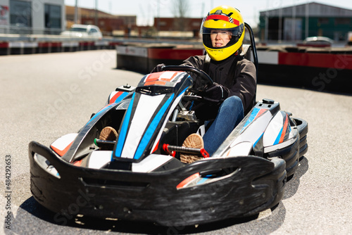 Young positive female in helmet driving car for karting in sport club outdoor © JackF