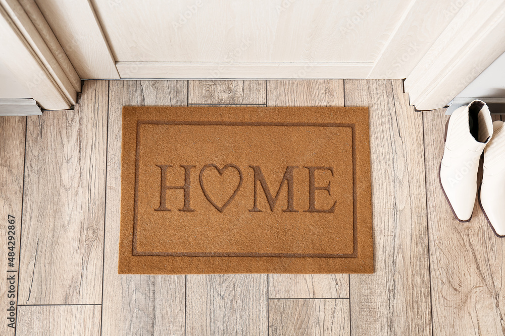 Stylish mat with word HOME near light wooden door in hallway - obrazy, fototapety, plakaty 