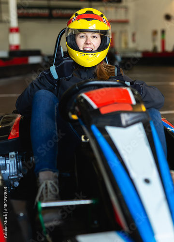 Positive woman with helmet sitting in car for karting in sport club
