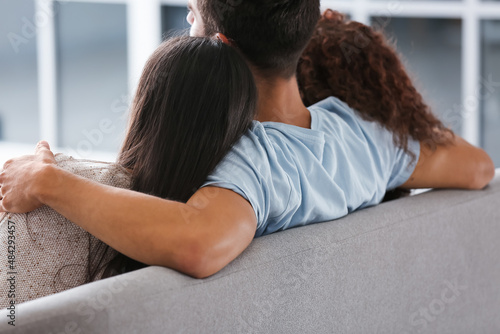 Man and two beautiful women sitting on sofa. Polyamory concept