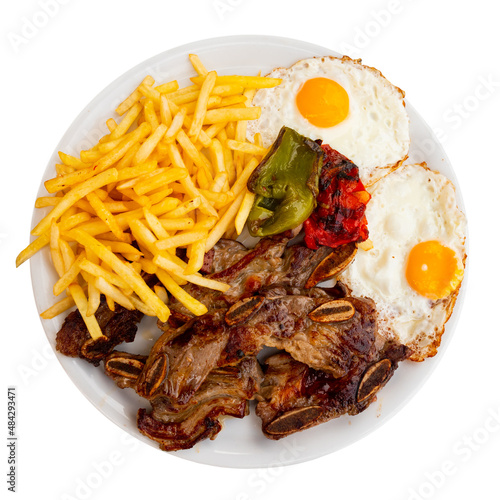 Appetizing grilled veal spare ribs churrasco with garnish of french fries, fried eggs and baked peppers. Combination meal concept. Spanish cuisine. Isolated over white background