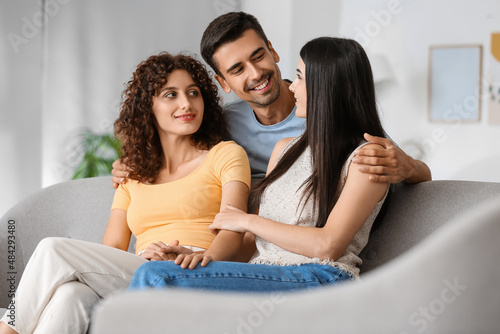 Man with two beautiful women at home. Polyamory concept