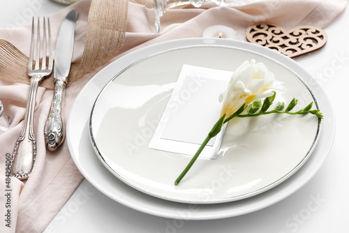 Beautiful table setting for wedding, flowers and blank card on light background