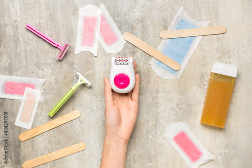 Female hand with epilator and different supplies for hair removal on grunge background