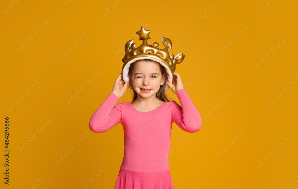Cute girl in inflatable crown on yellow background. Little princess Cute girl in inflatable crown on yellow background. Little princess