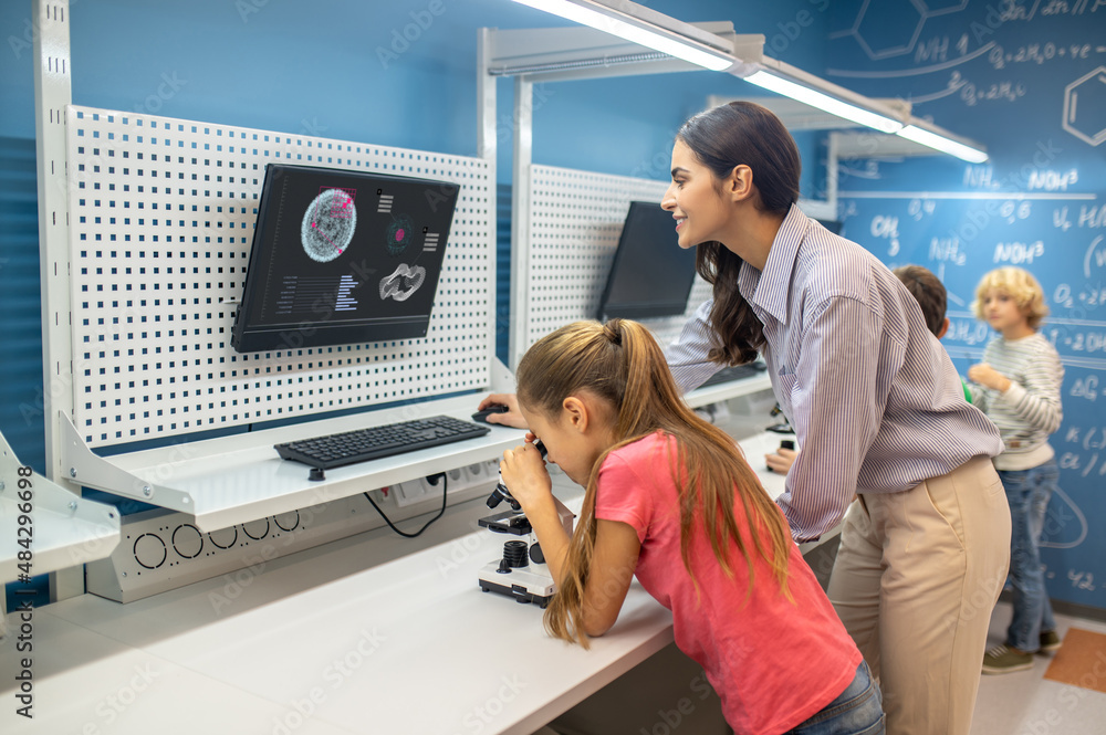 Woman looking at charging board and girl near microscope Woman looking at charging board and girl near microscope