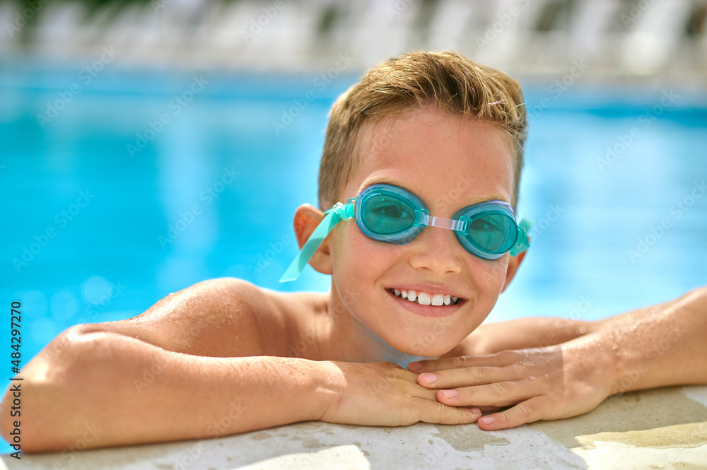 Boy in swimming goggles in pool looking at camera