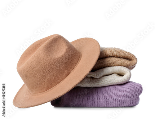 Stack of stylish sweaters and felt hat on white background