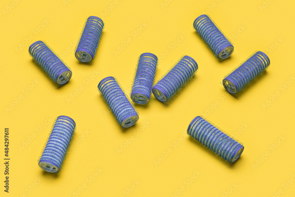 Fototapeta premium Blue hair rollers scattered on yellow background for hair styling and beauty salon concepts, these classic hair tools are used for creating curls and volume, essential for personal grooming and salon