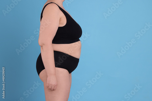 Overweight woman in underwear on light blue background, closeup. Space for text