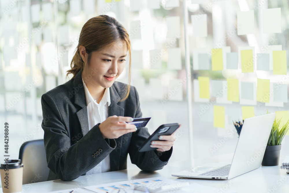 Young businesswoman with smartphone, credit card and laptop at desk in the office Young businesswoman with smartphone, credit card and laptop at desk in the office
