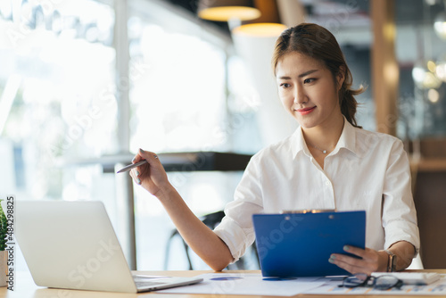 Front view of a happy employee comparing report online with a computer sitting in a desk at office
