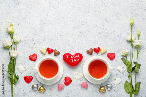 Tasty chocolate candies in shape of heart, cups with tea and flowers on light background. Valentine's Day celebration