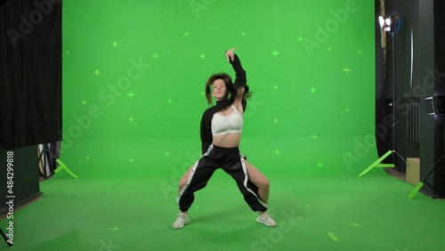 A young woman dancing on a green screen background. Attractive girl making content for social media. Modern blogger creating a master class. Chroma key