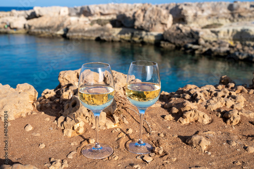 Two glasses of white dry white wine served on rocks in blue sea bay near Protaras touristic town on Cyprus