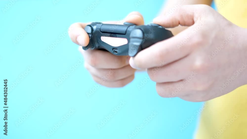 Male hands holding video game joystick on blue background, side view. Male hands holding video game joystick on blue background, side view.