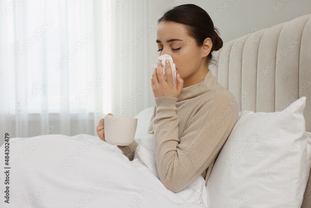 Sick young woman with cup of hot drink and tissue in bed at home, space for text Sick young woman with cup of hot drink and tissue in bed at home, space for text