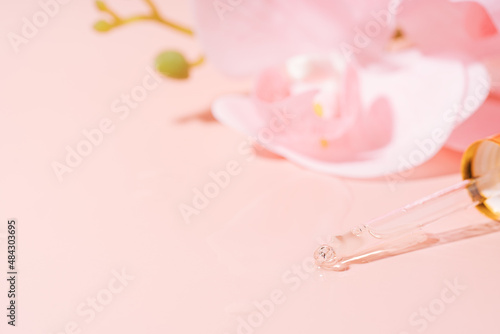Orchid and pipette filled with liquid on pink background.