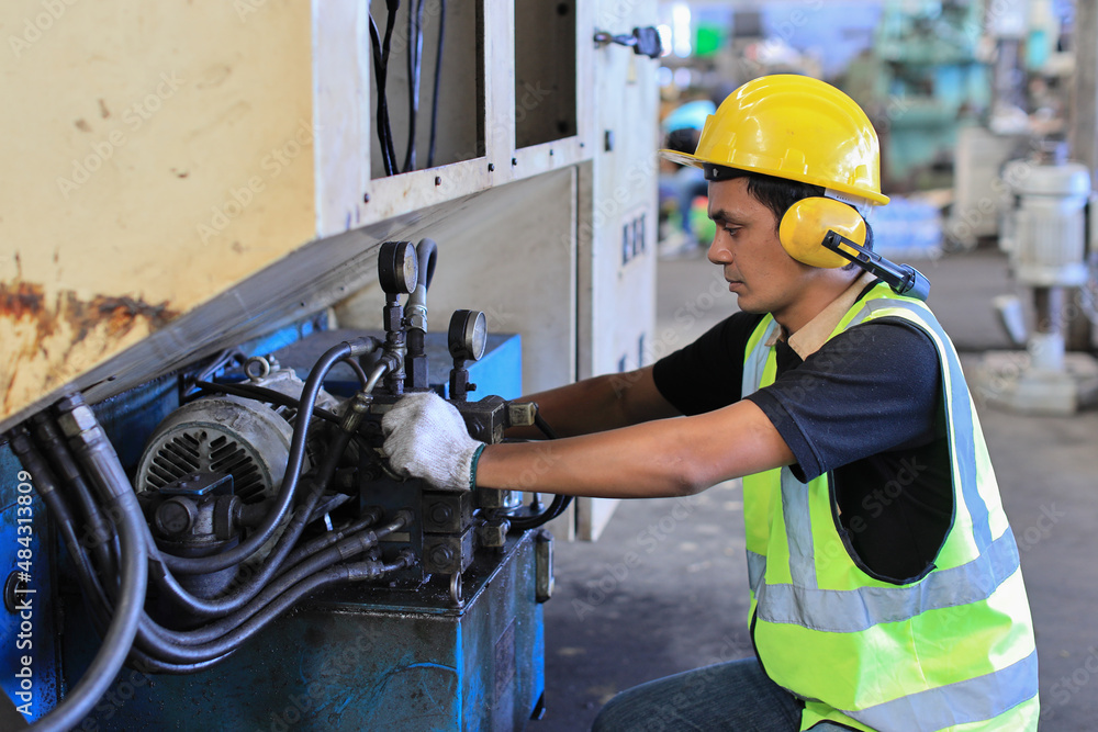 Fototapeta premium Technician engineer or worker in protective uniform standing and using computer while controlling operation or checking industry machine process with hardhat at heavy industry manufacturing factory