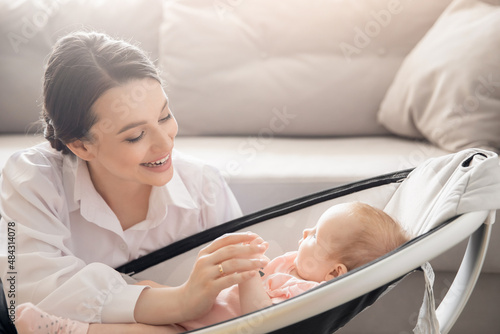 Mom holds little infant daughter by hand in automatic cradle for sleeping, sun light. Concept Morning with newborn baby