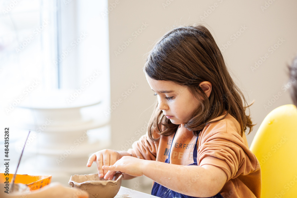 Cute little kid playing with modeling clay in pottery workshop, craft and clay art, child creative activities, education in Arts Cute little kid playing with modeling clay in pottery workshop, craft and clay art, child creative activities, education in Arts