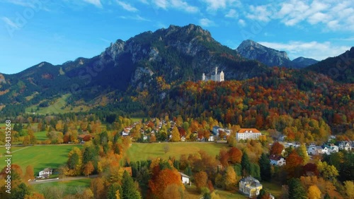 Relaxing view of drone flying over village houses towards castle on hill over scenic autumn field in the afternoon near the Neuschwanstein Castle in Germany, Europe, wide view