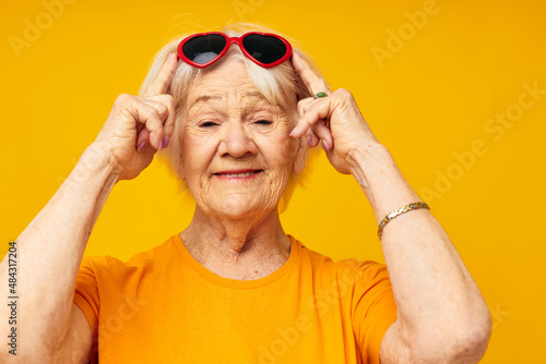 smiling elderly woman in casual t-shirt sunglasses yellow background