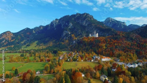 View of drone punching in while slowly flying over village houses towards castle on hill over scenic autumn field in the afternoon near the Neuschwanstein Castle in Germany, Europe, wide view photo