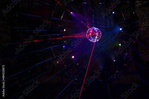 Mirrored Disco Ball and bright beams at the night party. Party attribute reflects Lazer lights. Abstract background with defocused rays. Night club atmosphere. Installation at Vilnius light festival