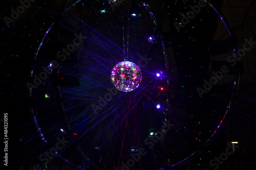 Mirrored Disco Ball and bright beams at the night party. Party attribute reflects Lazer lights. Abstract background with defocused rays. Night club atmosphere. Installation at Vilnius light festival