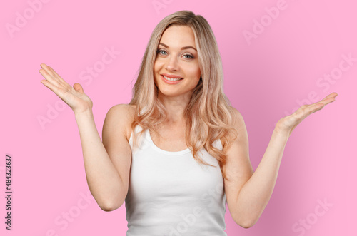 Portrait of uncertain young woman with blonde hair standing with raised arms isolated on color background