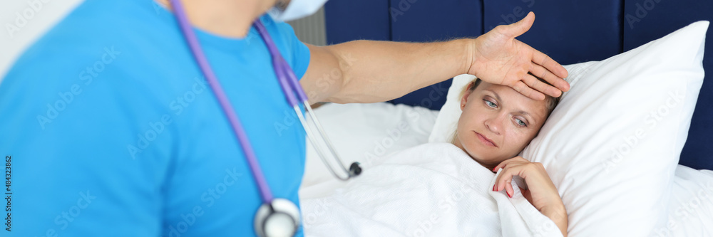 Doctor holds hand on forehead of lying woman on bed with fever