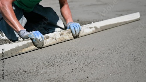 Close up of man builder placing screed rail on the floor covered with sand-cement mix at construction site on the roof. Male worker leveling surface with straight edge while screeding floor. photo