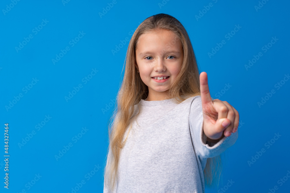 Cheerful teenage girl pointing finger at camera on blue background Cheerful teenage girl pointing finger at camera on blue background