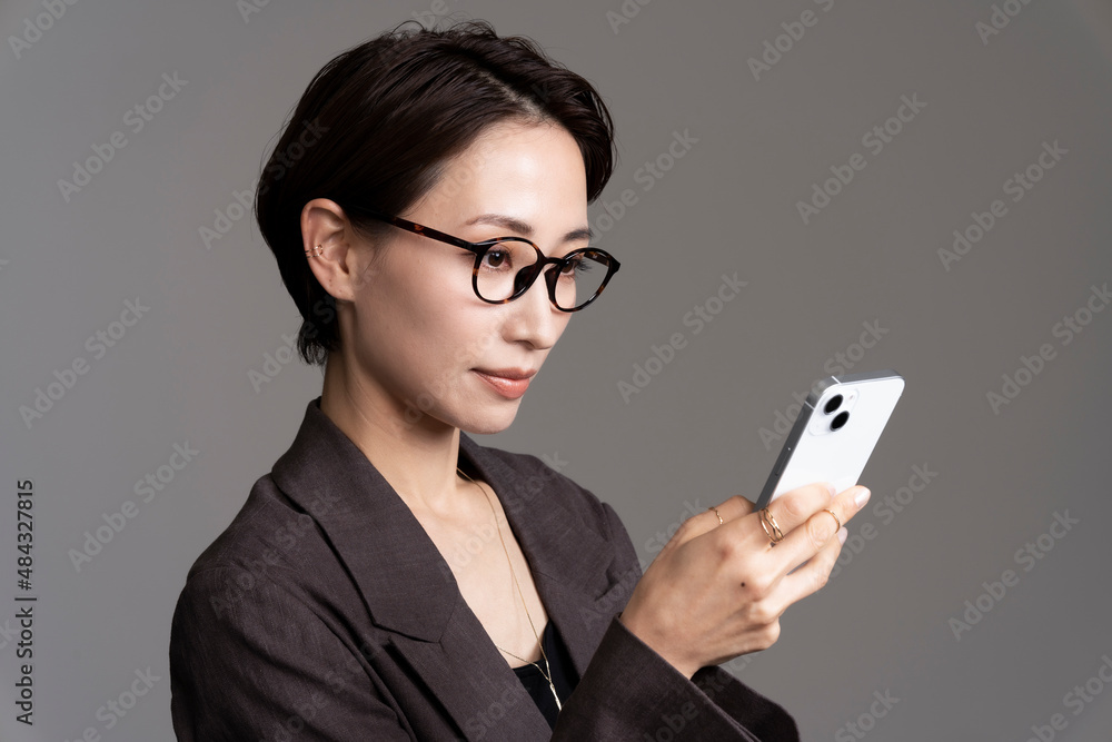 スマートフォンをみている日本人女性/グレー背景スタジオ撮影