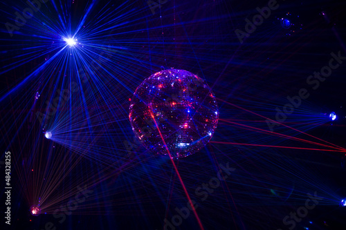 Mirrored Disco Ball and bright beams at the night party. Party attribute reflects Lazer lights. Abstract background with defocused rays. Night club atmosphere. Installation at Vilnius light festival