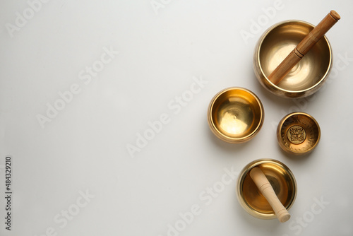 Golden singing bowls and mallets on white background, flat lay. Space for text