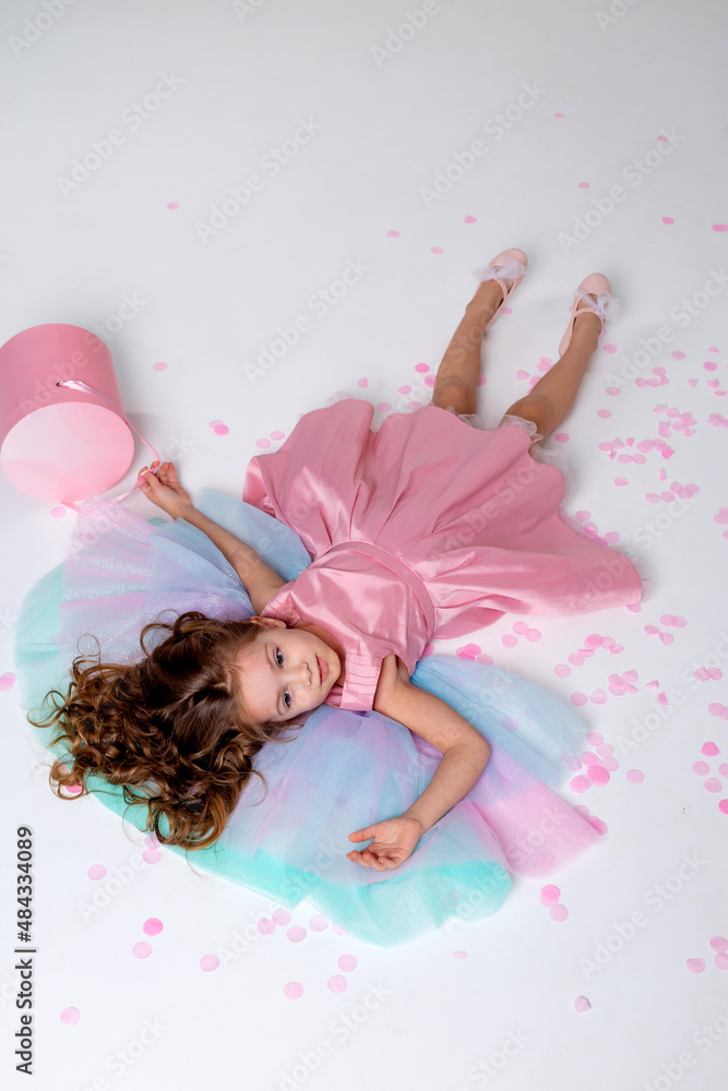 beautiful little girl in a chic pink dress lies on the floor strewn ...