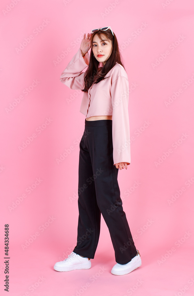 Portrait closeup studio shot of Asian young beautiful hipster female teenager model in casual long sleeve shirt street wears and sunglasses standing posing smiling look at camera on pink background Portrait closeup studio shot of Asian young beautiful hipster female teenager model in casual long sleeve shirt street wears and sunglasses standing posing smiling look at camera on pink background
