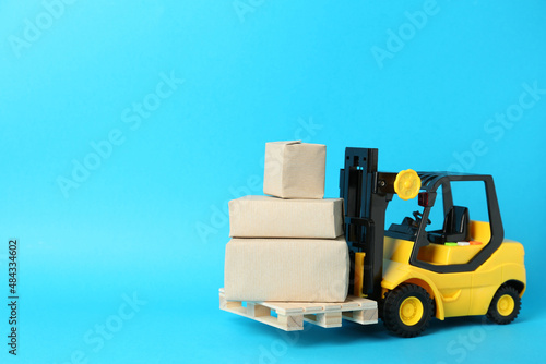 Toy forklift with wooden pallet and boxes on light blue background, space for text