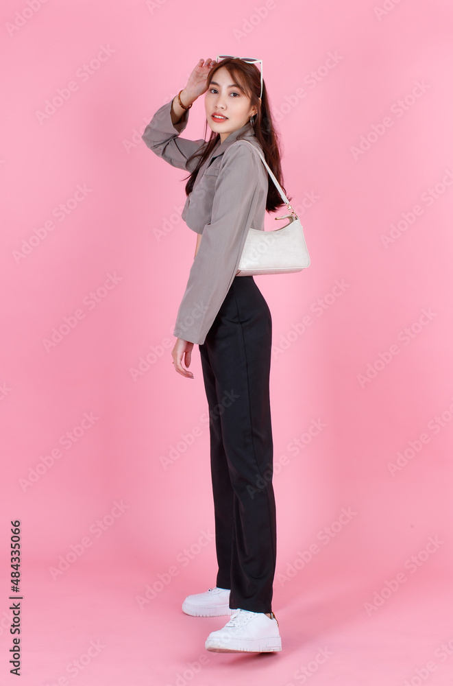 Portrait studio shot of Asian trendy fashionable female hipster teen model in casual crop top street wears jacket sunglasses sneakers holding handbag purse look at camera on pink background. Portrait studio shot of Asian trendy fashionable female hipster teen model in casual crop top street wears jacket sunglasses sneakers holding handbag purse look at camera on pink background.