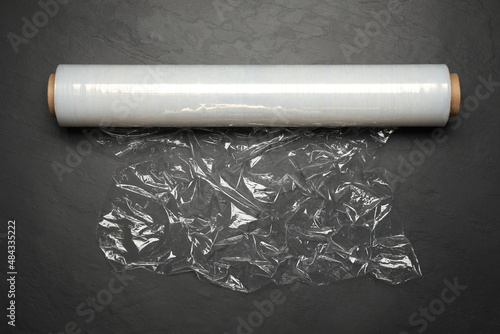 Roll of plastic stretch wrap film on black table, top view